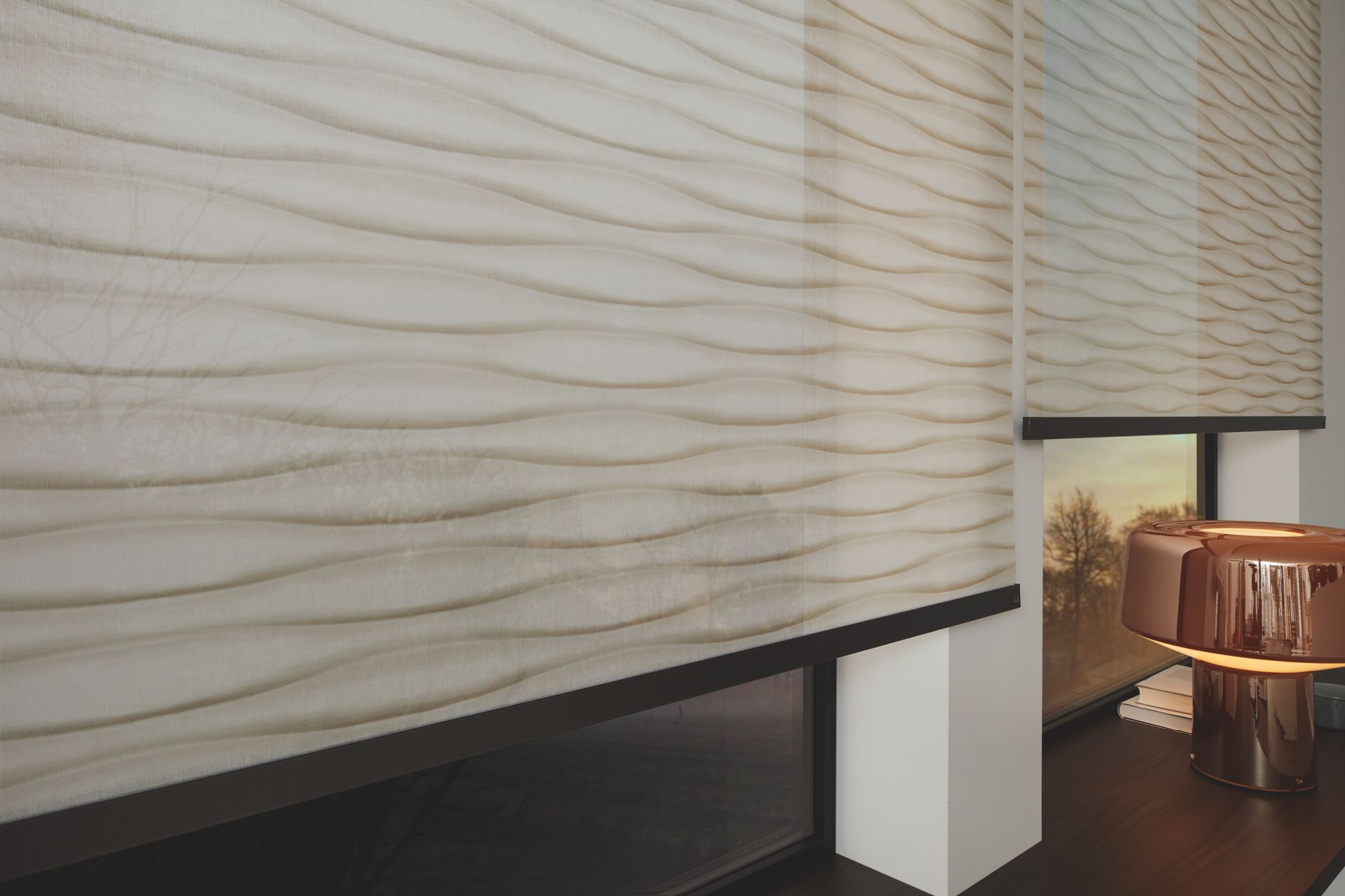 Beigefarbene Jalousien mit Wellenmuster, die ein Fenster teilweise bedecken.