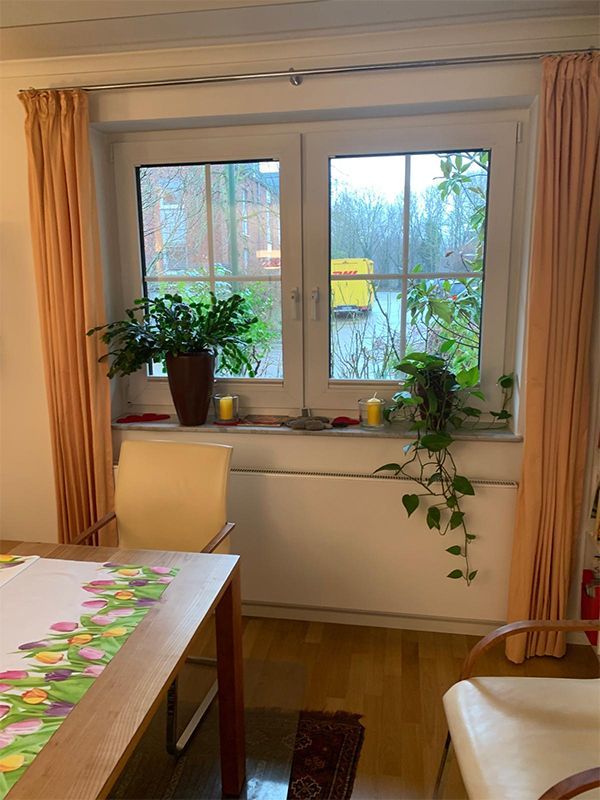 Esszimmer im Innenbereich mit einem Fenster mit Blick auf einen Garten. Rosa Vorhänge rahmen das Fenster, einen Tisch, Pflanzen und Stühle ein.