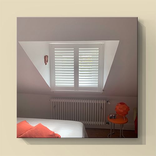 Schlafzimmer mit weißen Fensterläden, orangefarbenen Kissen und Stuhl.