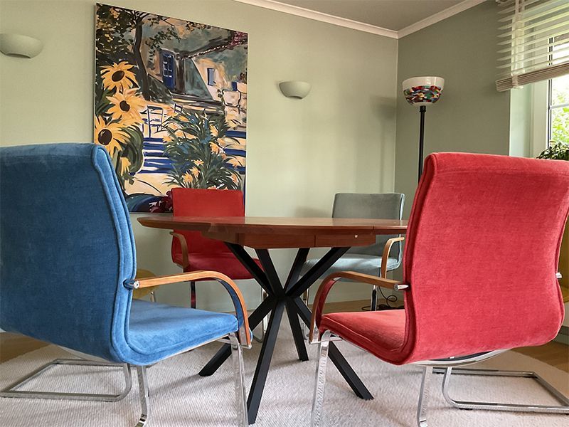 Runder Esstisch aus Holz mit vier bunten Stühlen in einem hellgrünen Raum.