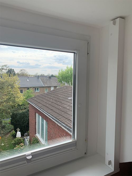 Weißer Fensterrahmen mit Blick auf Dächer, Bäume und Himmel.