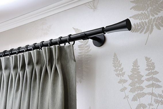 Schwarze Gardinenstange mit grauen Vorhängen vor einer weißen Wand mit Farntapete.