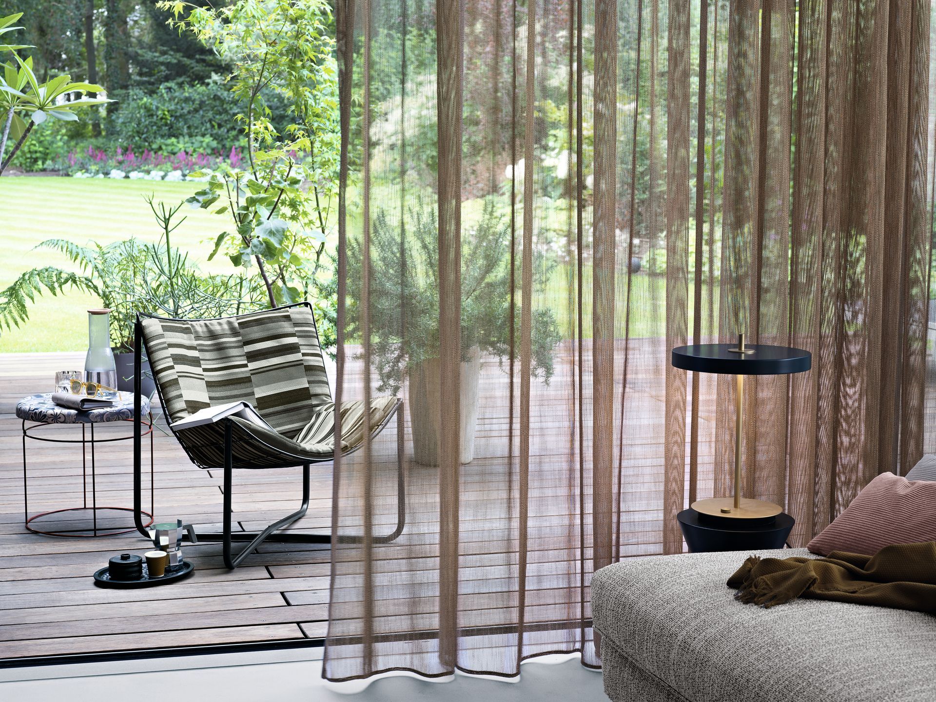 Durchsichtige braune Vorhänge vor einer Außenszene mit Stuhl, Pflanzen und einem kleinen Tisch.