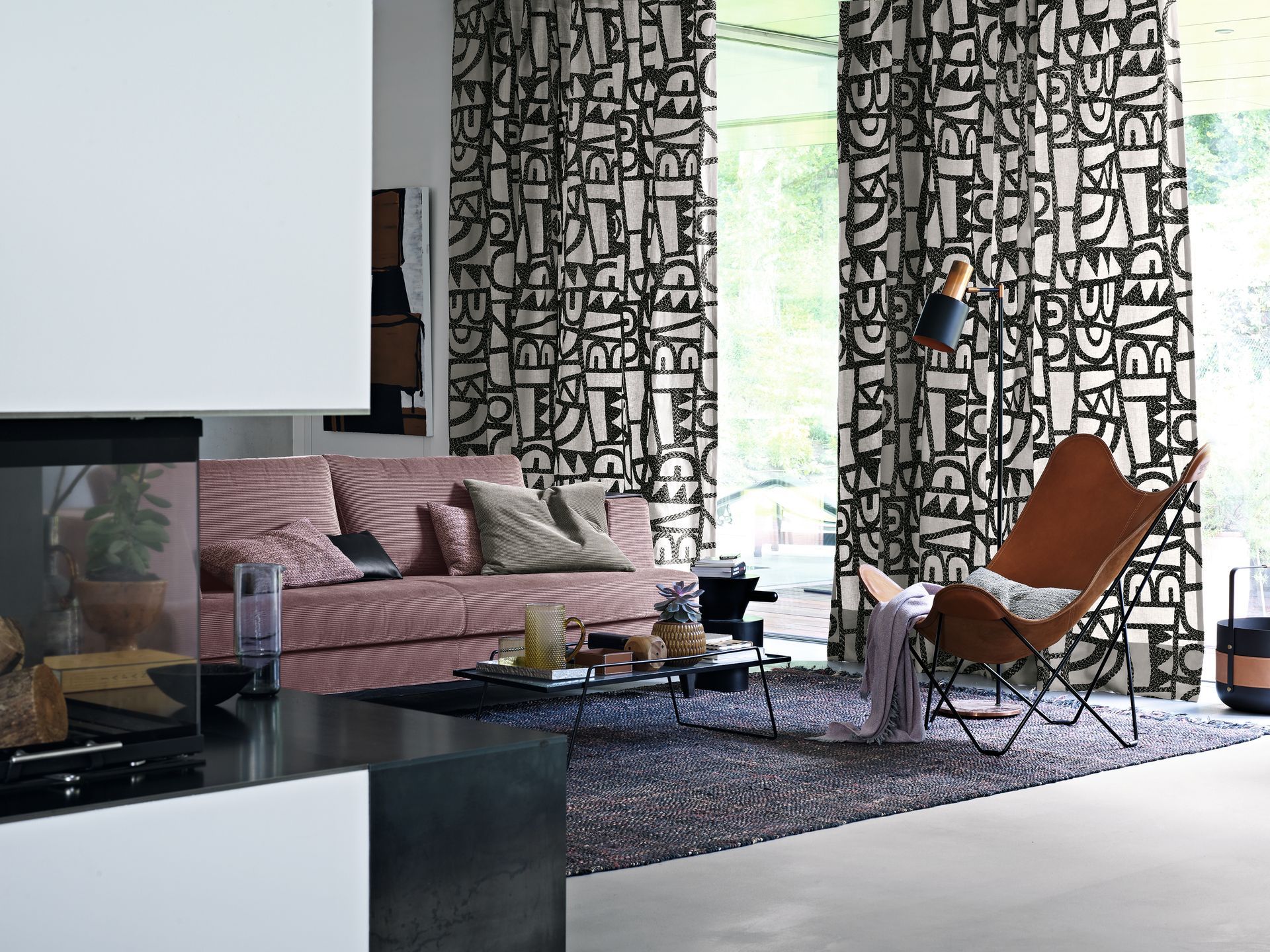 Wohnzimmer mit rosa Sofa, gemusterten Vorhängen, Ledersessel und dunklem Teppich.