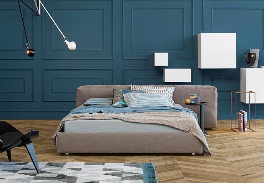 Schlafzimmer mit Bett, blauer Wandvertäfelung, moderner Kunst und Holzboden.