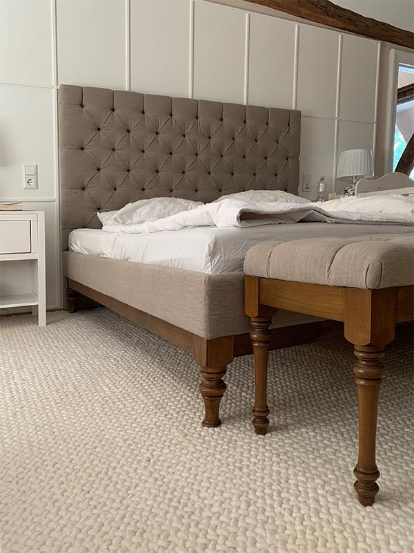 Beiges Bett mit gepolstertem Kopfteil und passender Bank auf weißem strukturiertem Teppich.