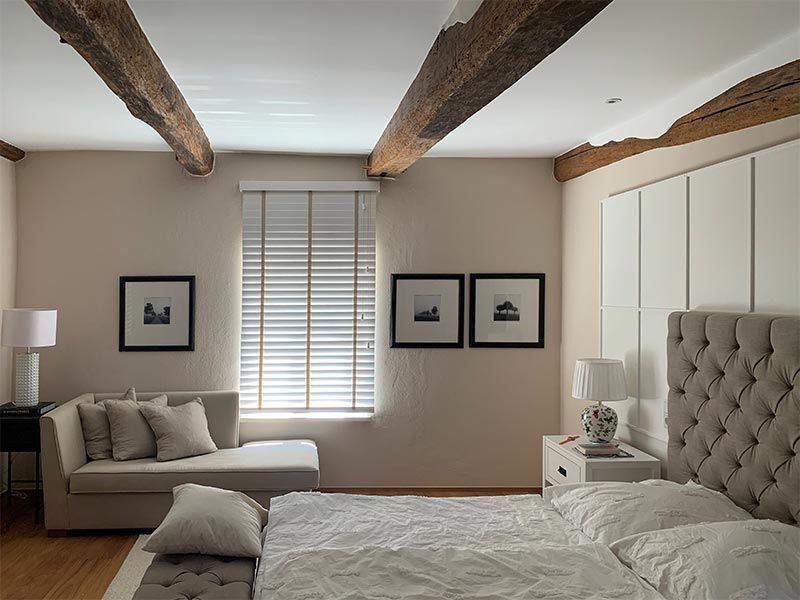 Schlafzimmer mit Bett, Chaiselongue, Kunst, Fenster und freiliegenden Holzbalken.