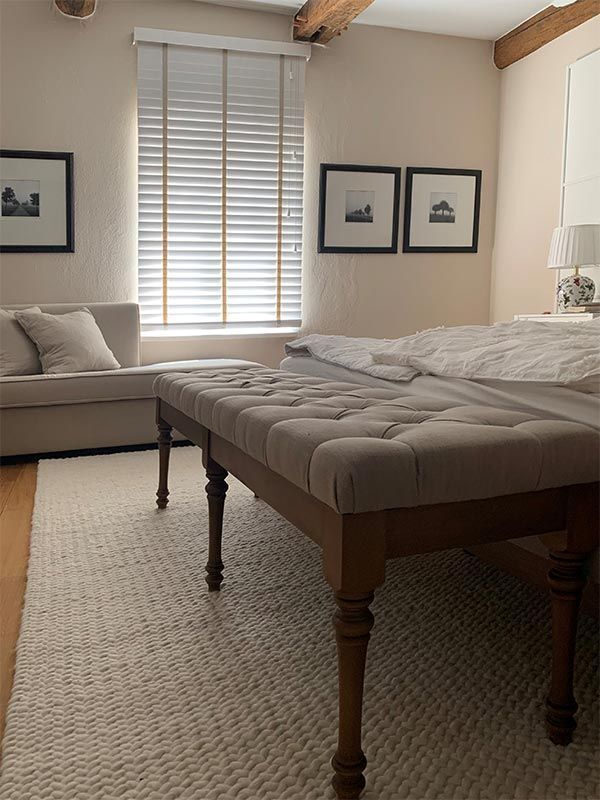 Schlafzimmer mit gepolsterter Bank, Bett, Sofa, Fenster mit Jalousien, gerahmten Bildern und Teppich.