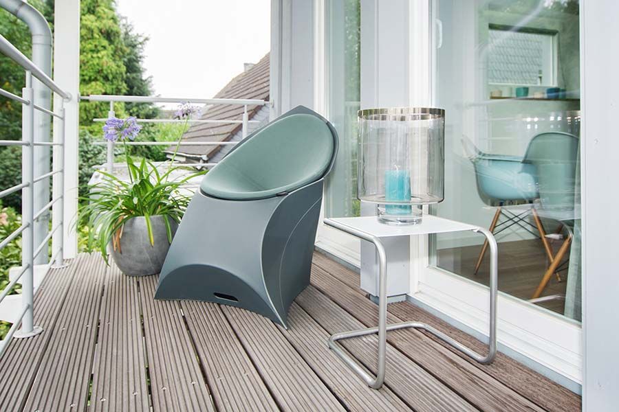 Ein moderner Außenbalkon mit einem grauen Stuhl, einem kleinen weißen Tisch und Topfpflanzen.