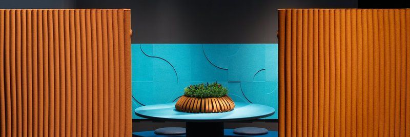 Ein Tisch mit einem Moos-Mittelstück, eingerahmt von orangefarbenen Paneelwänden vor einer blaugrünen Wand mit abstrakten Linien.