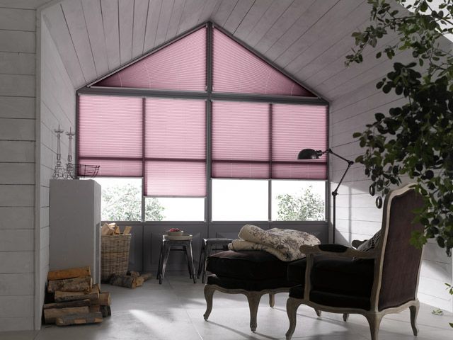 Rosa Plissees bedecken ein großes Fenster in einem hellen, gemütlichen Dachgeschoss.