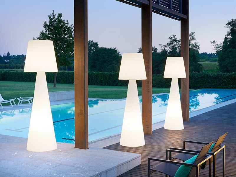 Drei beleuchtete Außenlampen neben einem Pool vor einer Holzkonstruktion in der Abenddämmerung.