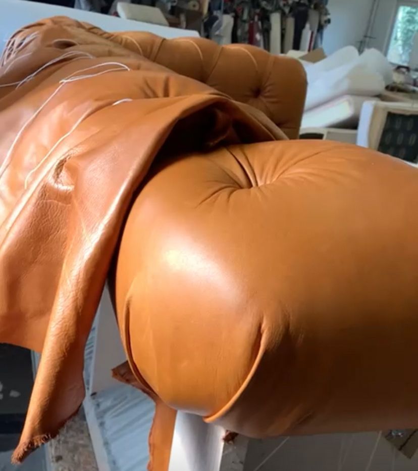 Hellbraune Lederpolsterung wird hergestellt; Näh- und Formdetails sind sichtbar.