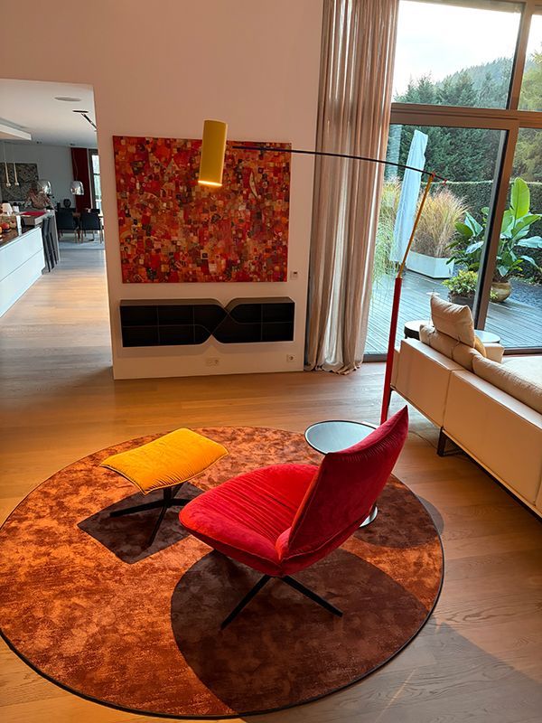 Roter Sessel auf einem runden Teppich neben einer modernen Stehlampe, Kunstwerken und großen Fenstern.