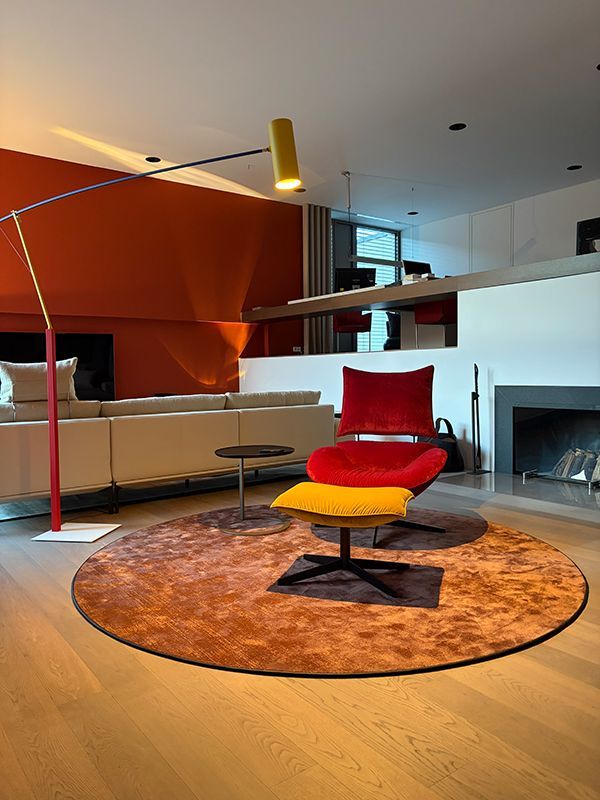 Modernes Wohnzimmer mit orangefarbener Akzentwand, rot-gelbem Sessel und rundem Teppich.