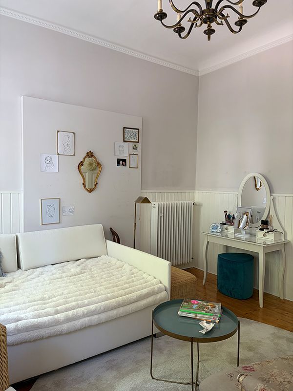 Gemütliches Schlafzimmer mit weißem Tagesbett, Schminktisch, Heizkörper, rundem Glas-Couchtisch und Kronleuchter.