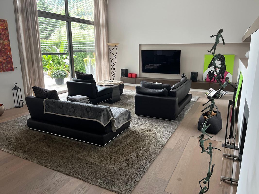 Wohnzimmer mit schwarzen Ledermöbeln, großem Fernseher, Kunstwerken und Teppich.