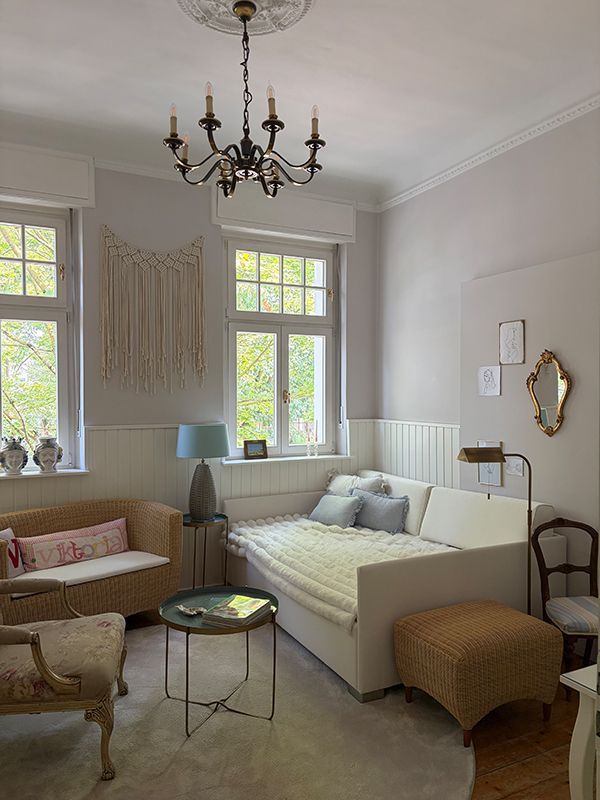 Helles, elegantes Wohnzimmer mit Tagesbett, Sessel, Kronleuchter und großen Fenstern mit weichen Vorhängen.