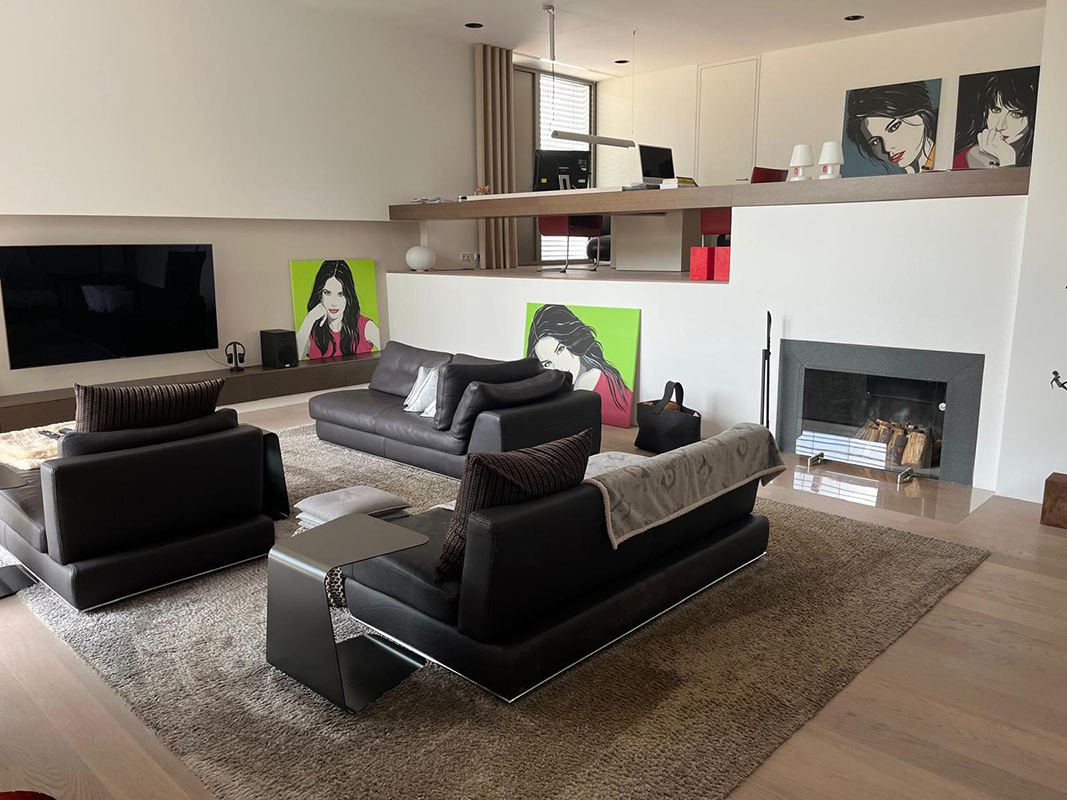 Modernes Wohnzimmer mit schwarzen Ledermöbeln, Kamin und Kunstwerken an weißen Wänden.