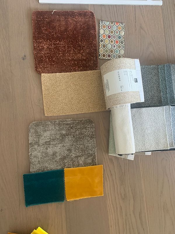 Verschiedene Stoff- und Teppichmuster in Braun-, Gold-, Grün- und Blautönen auf einem Holzboden.