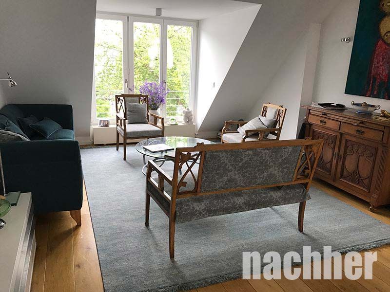 Wohnzimmer mit blaugrünem Sofa, antiken Möbeln, blauem Teppich und großem Fenster.