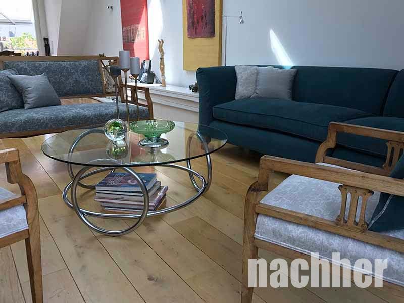 Wohnzimmer mit blauem Sofa, Holzstühlen, Couchtisch aus Glas und Hartholzböden.
