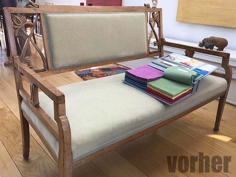 Holzbank mit gepolsterter Sitzfläche, Stoffmustern darauf und einer Nashornskulptur auf der Armlehne.