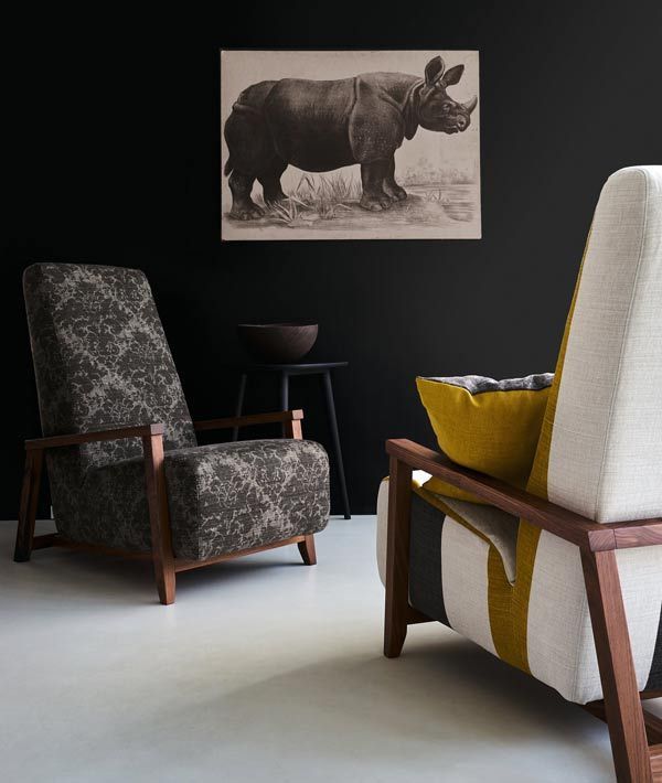 Zwei gemusterte Sessel in einem Raum mit schwarzen Wänden, einem Nashornbild und einem Hocker.
