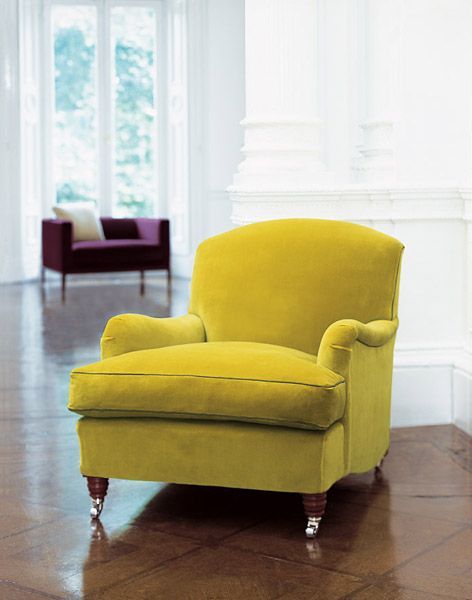 Gelber Samtsessel mit geschwungener Rückenlehne in einem hellen Raum. Im Hintergrund ist ein weiteres Sofa zu sehen.