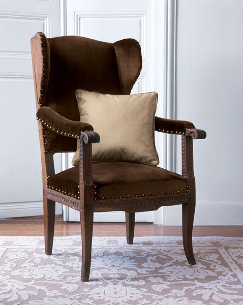 Brauner Samtsessel mit hellbraunem Kissen, auf einem gemusterten Teppich.