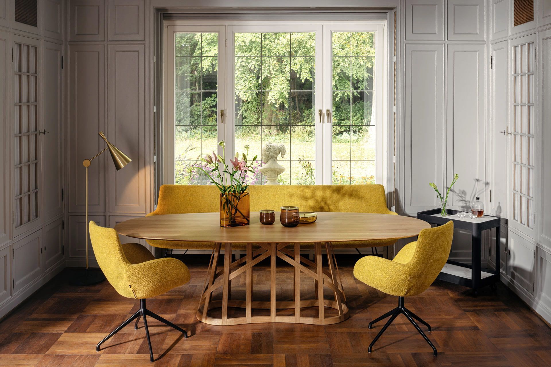 Esszimmer mit gelben Stühlen und Bank, Holztisch und großem Fenster mit Blick ins Grüne.