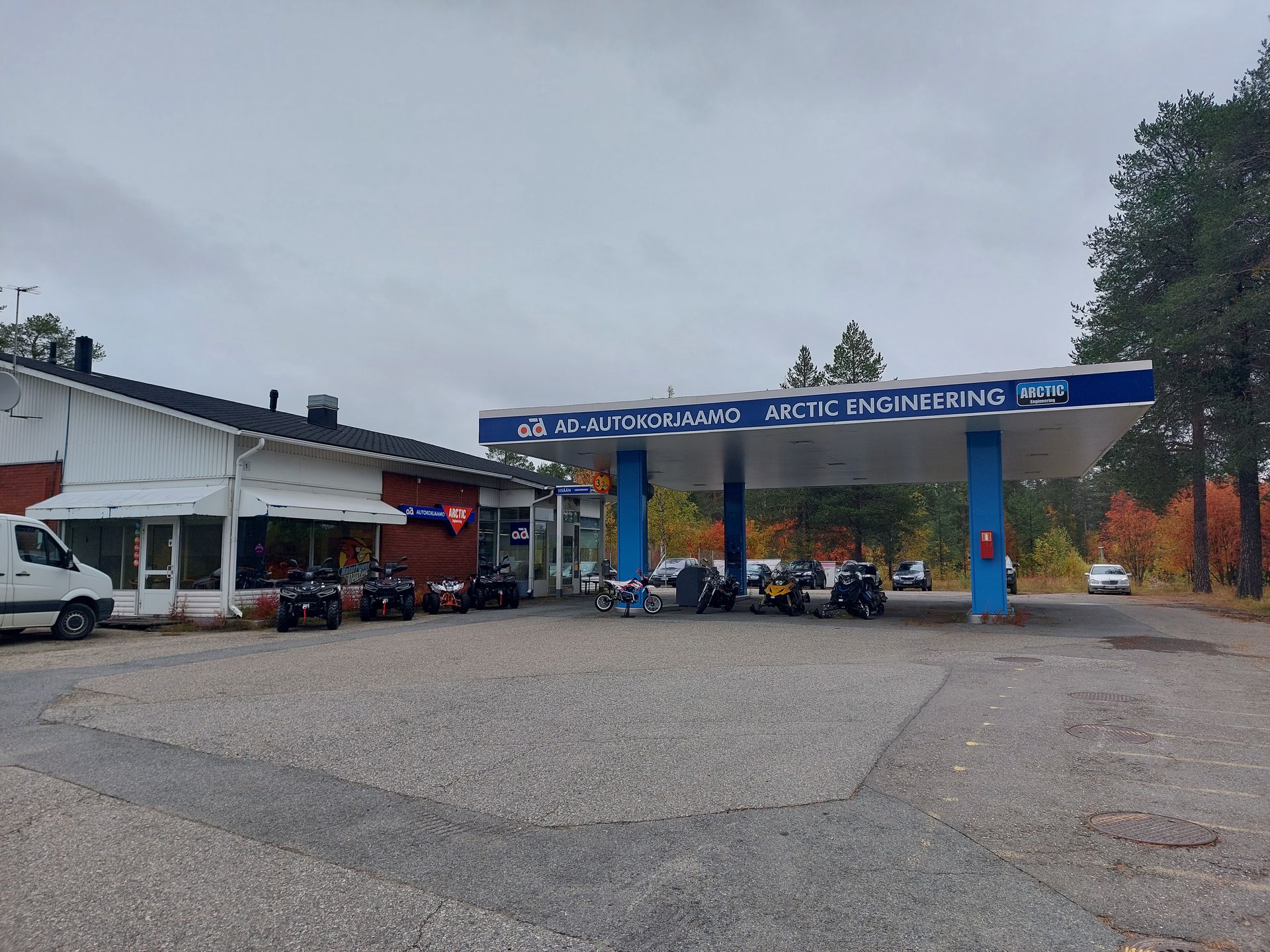 Sorakentän huoltoasema pilvisen taivaan alla, useita moottoripyöriä pysäköitynä sinivalkoisen huoltokatoksen alle.