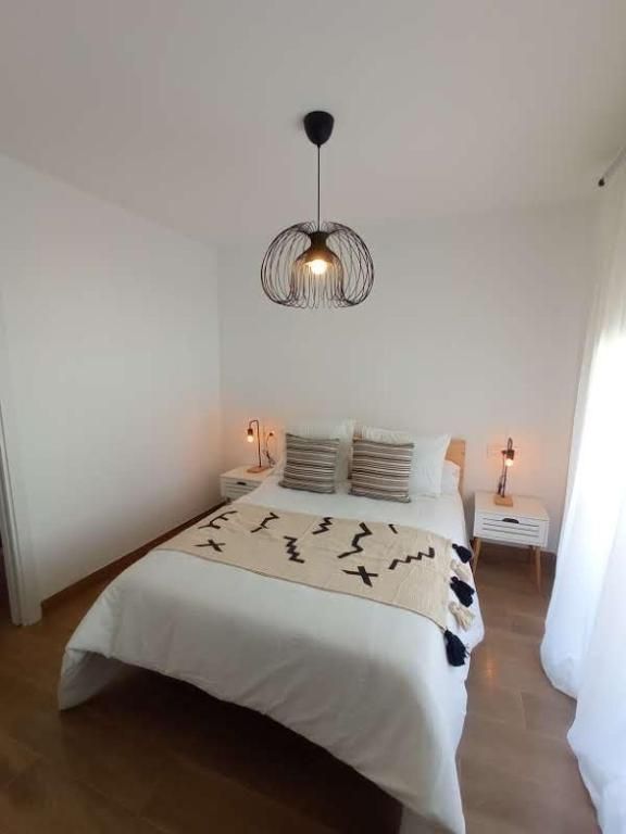 Un dormitorio con cama, mesita de noche, lámpara y ventana.