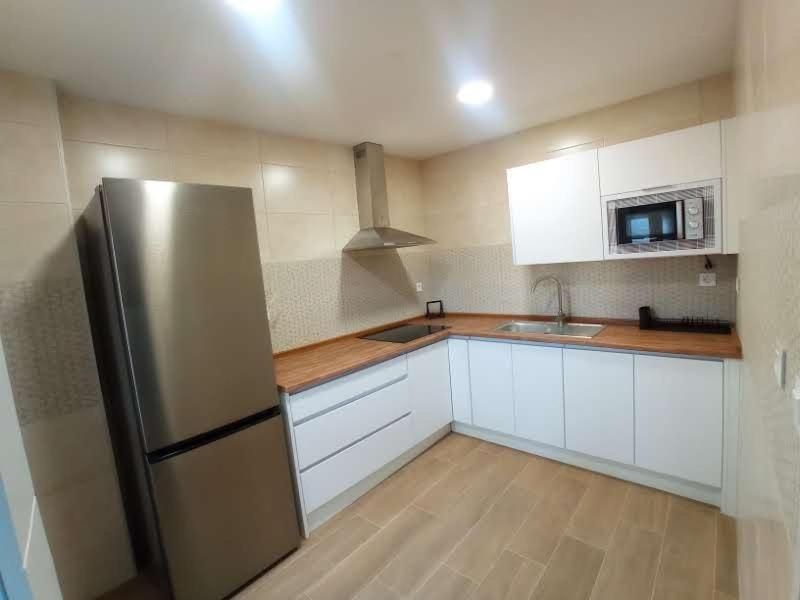 Una cocina con gabinetes blancos, un refrigerador de acero inoxidable, un fregadero y un microondas.
