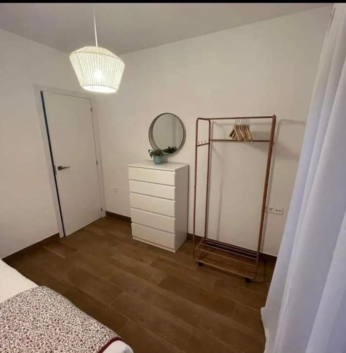 Un dormitorio con cama, tocador, espejo y perchero.