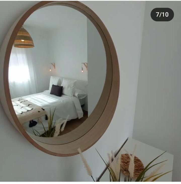 Un espejo redondo muestra un dormitorio con una cama y almohadas.