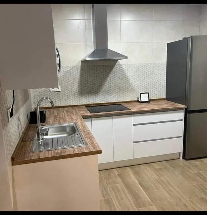 Una cocina con fregadero, refrigerador, estufa y campana extractora.