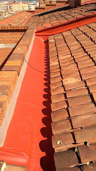 Un techo con tejas rojas y un canalón rojo sobre él.