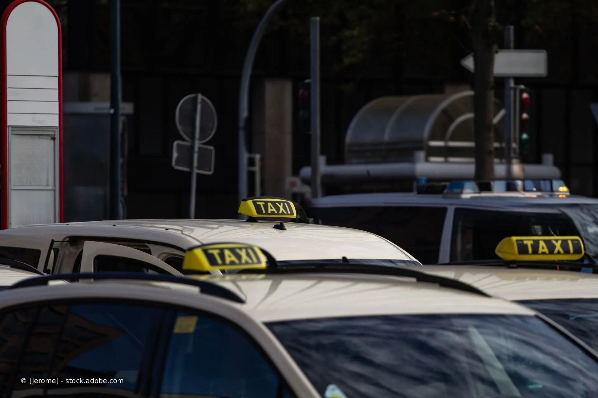 Mehrere beige Taxis mit gelben „TAXI“-Dachschildern parken in einer Stadtstraße.
