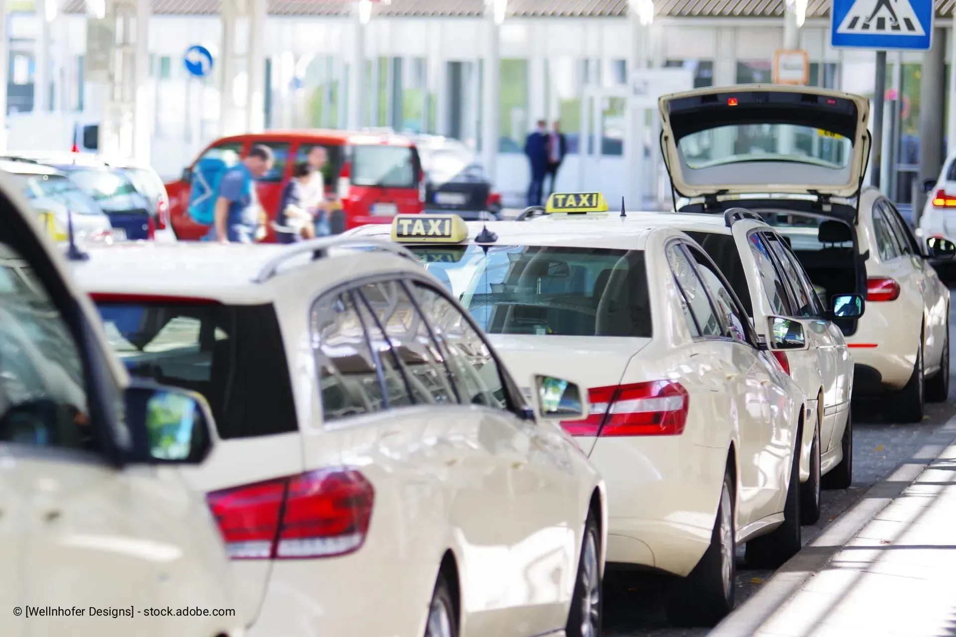 Eine Reihe weißer Taxis wartet in einer Schlange an einem Flughafenterminal.