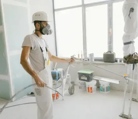 Un hombre que lleva una máscara está rociando pintura en una pared de una habitación.