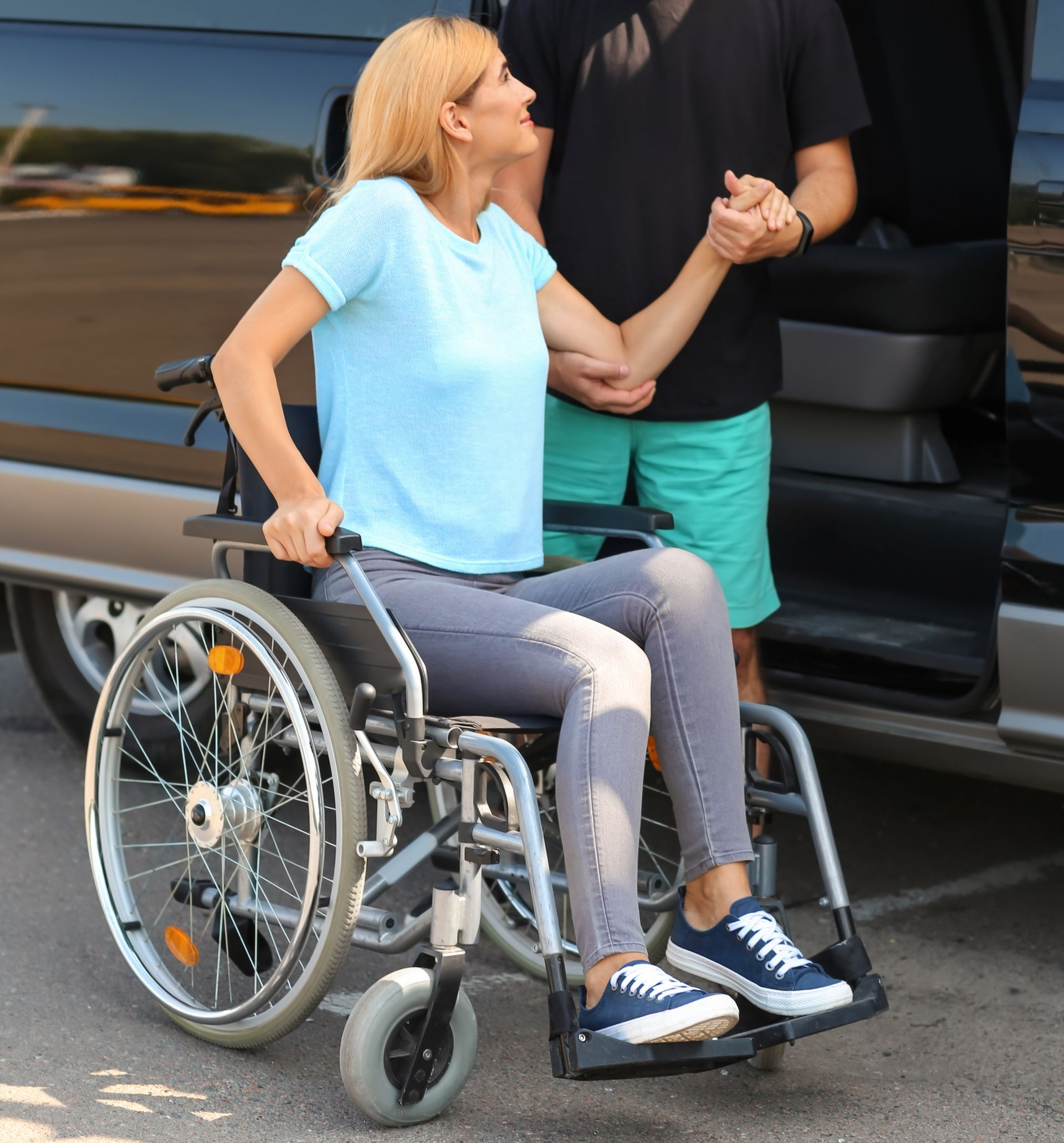 Une femme en fauteuil roulant est aidée par une personne qui sort du véhicule.