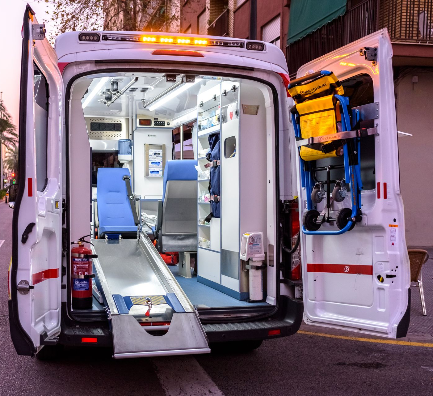 Intérieur d'une ambulance avec portes ouvertes, montrant du matériel médical, des sièges et une rampe.