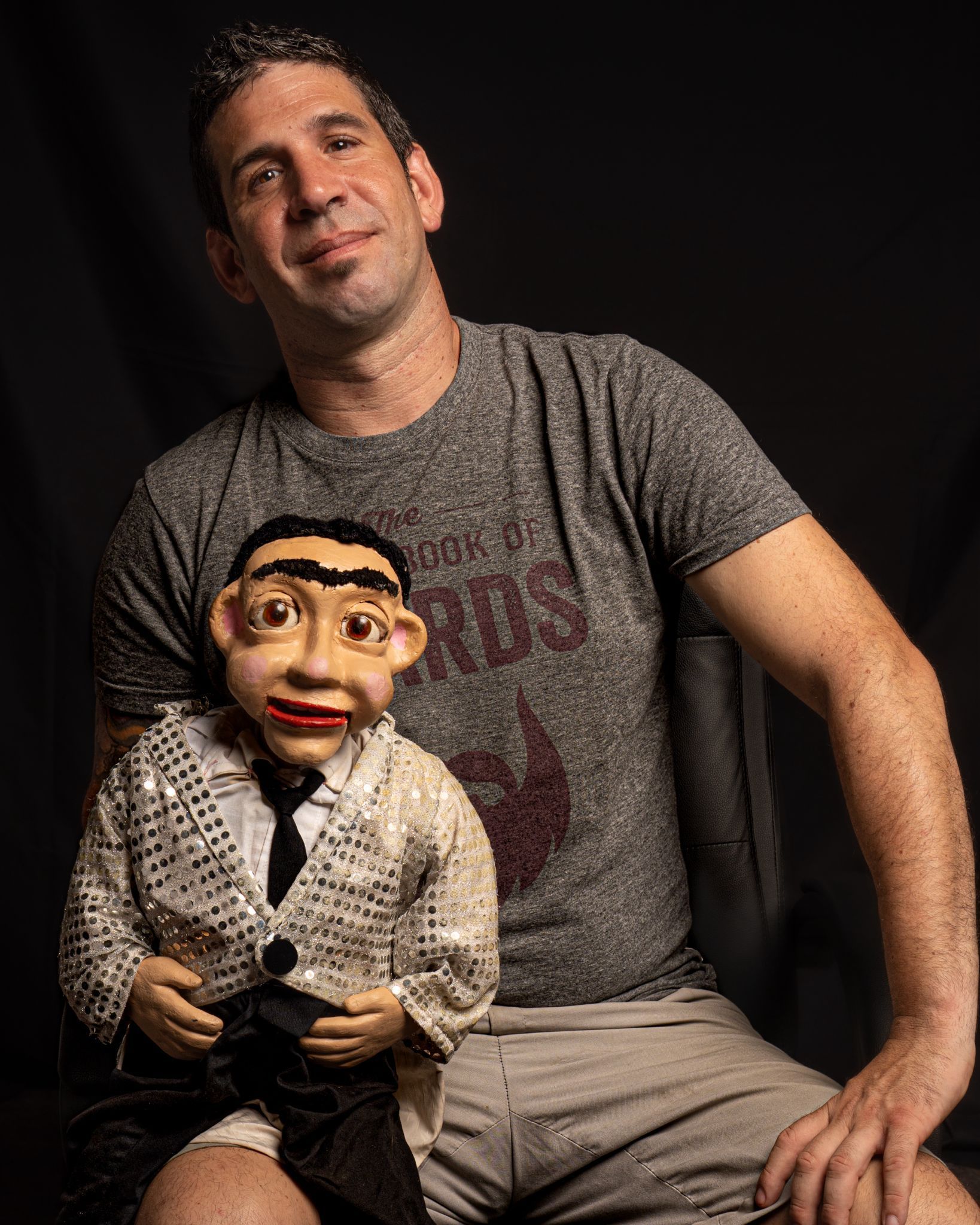 Un hombre está sentado junto a una marioneta en su regazo.