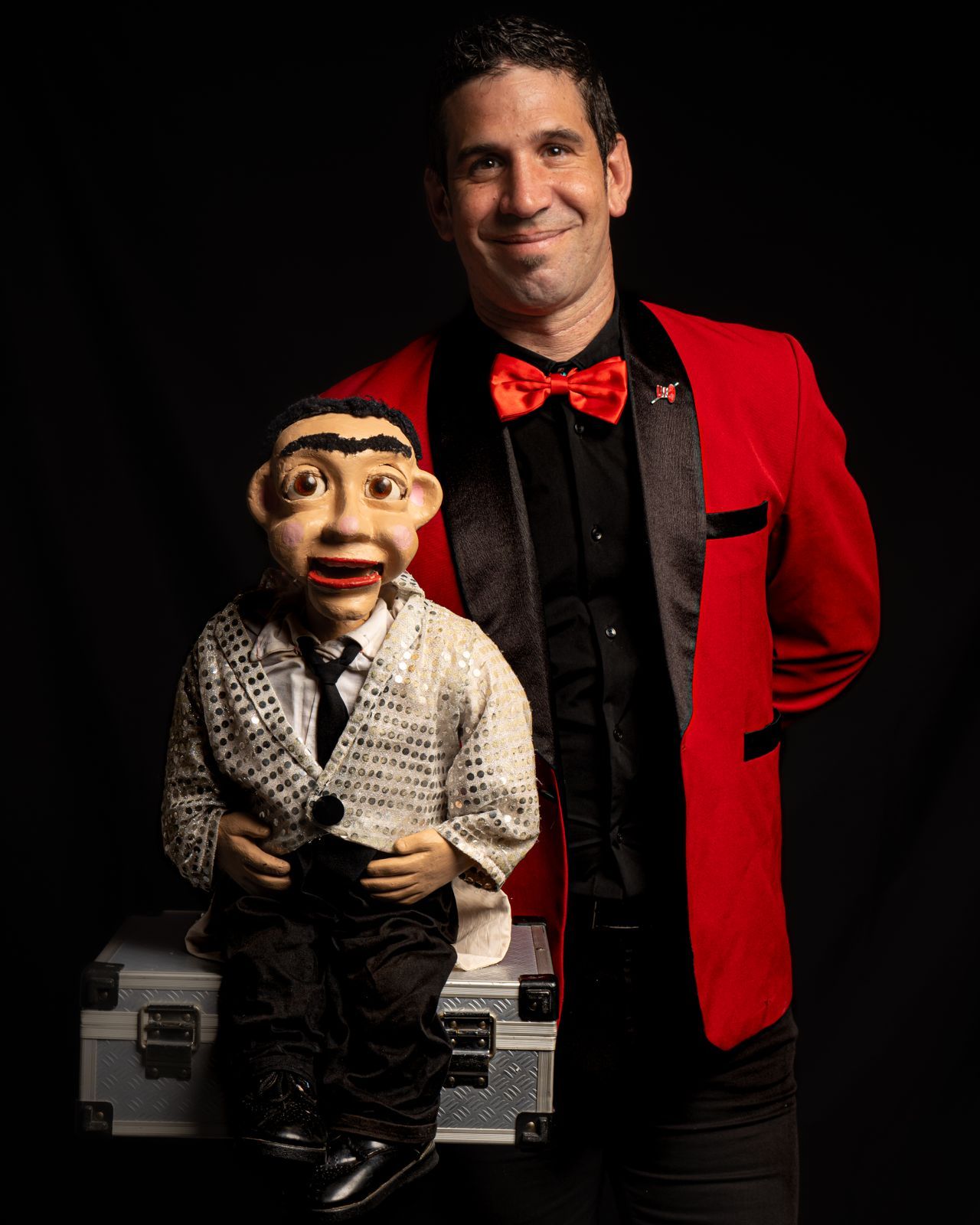 Un hombre con una chaqueta roja está de pie junto a una marioneta.