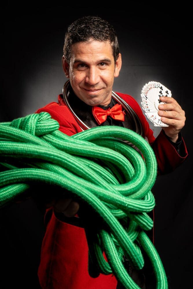 Un hombre con una chaqueta roja sostiene una gran cuerda verde y juega a las cartas.