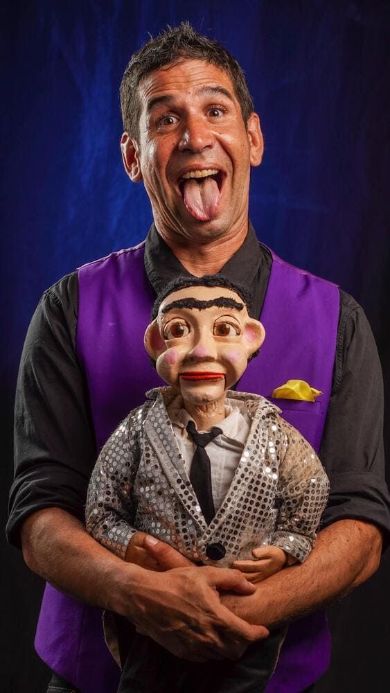 Un hombre con un chaleco morado sostiene una marioneta.