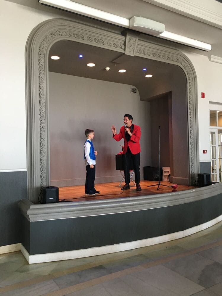 Un hombre con una chaqueta roja está de pie en un escenario hablando con un niño.