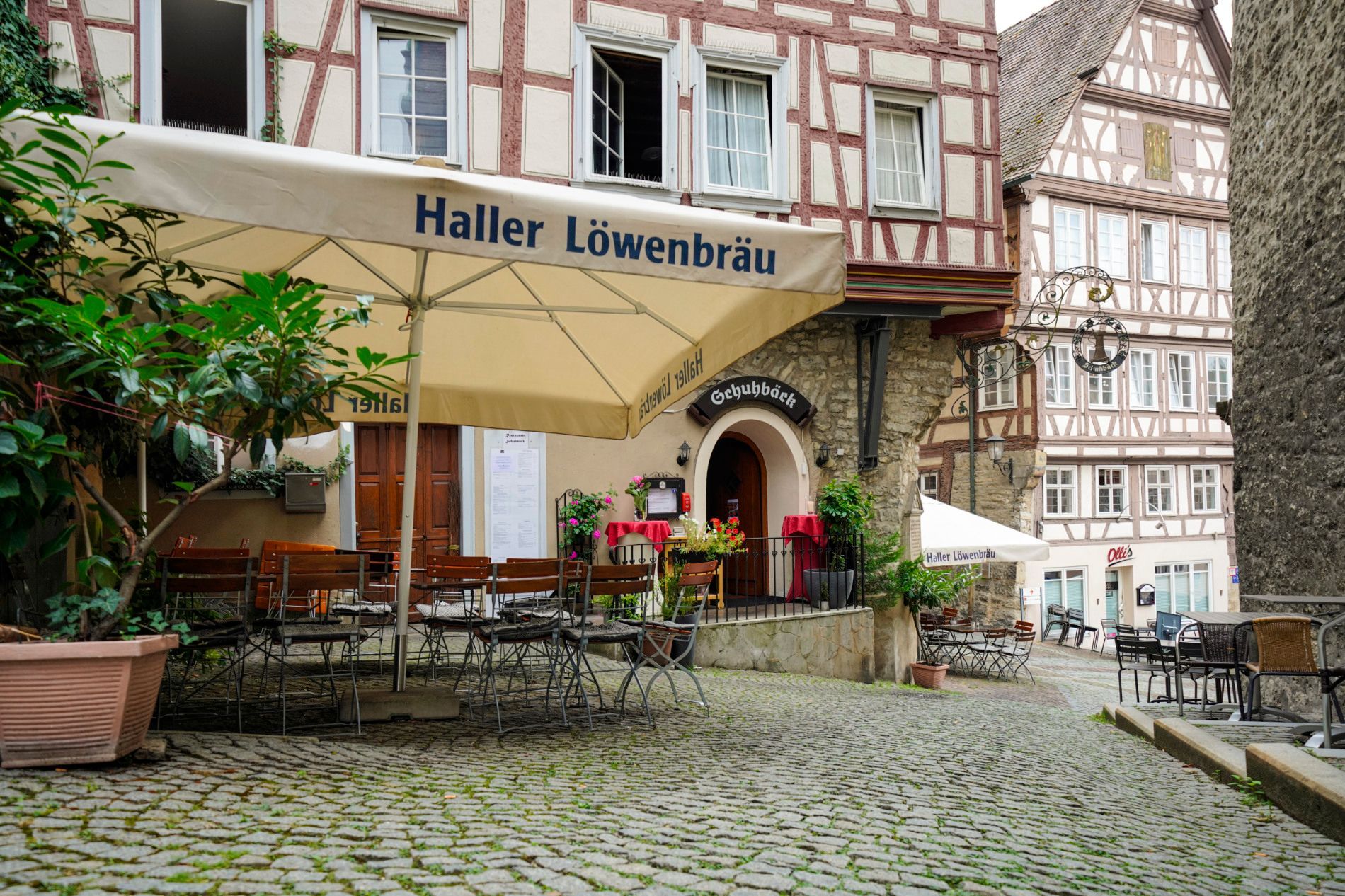 Restaurant Schuhbäck mit Tischen und Stühlen unter einem Sonnenschirm vor einem Gebäude.