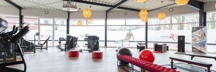 Ein Fitnessstudio mit vielen Trainingsgeräten und einer Bank.